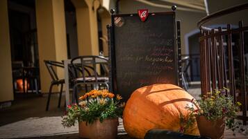 A chalkboard with writing, a pumpkin, and two flower pots on a brick-paved area.