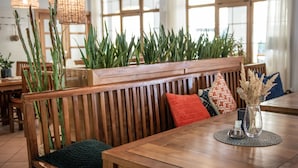 A wooden bench with a cushion, a table with a vase, and a row of green plants. - Resort-Restaurant Štilec (Kamenný Újezd)