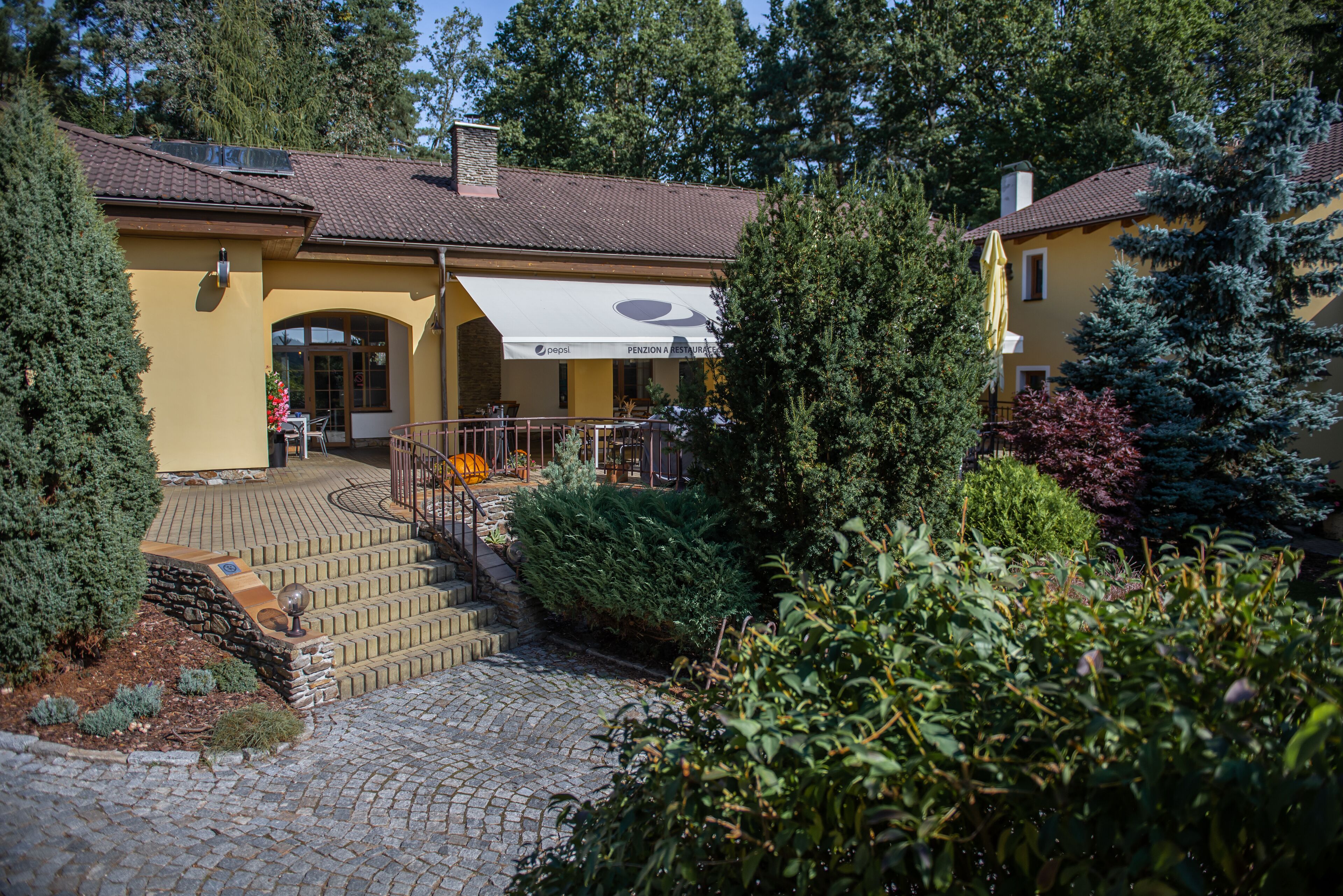 A yellow building with a tiled roof, a covered patio area, and a stone pathway leading to the entrance.