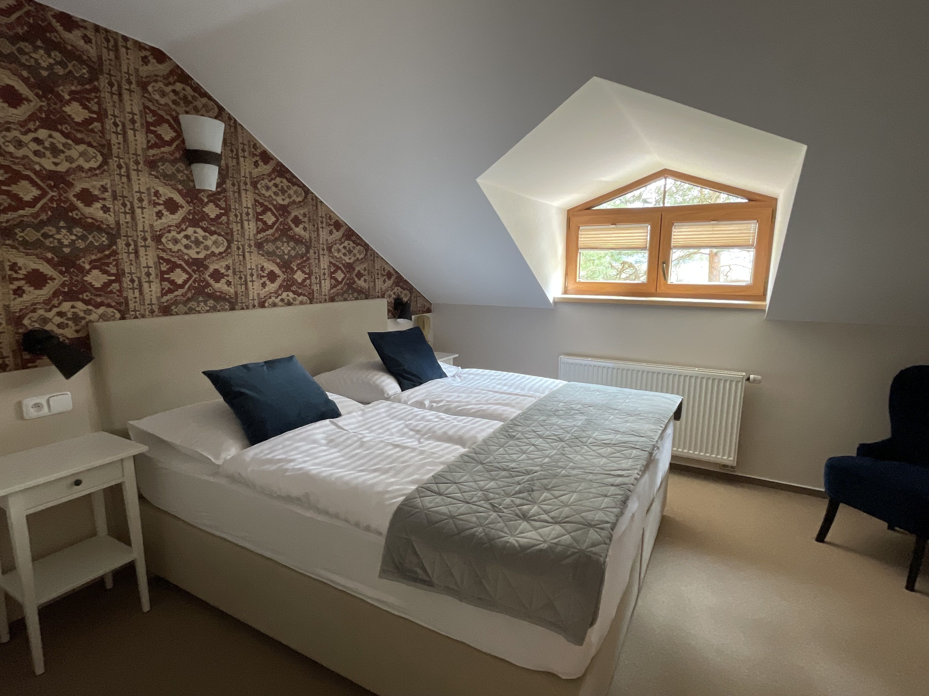 A bedroom with a bed, a nightstand, a chair, a window, and a patterned wall.