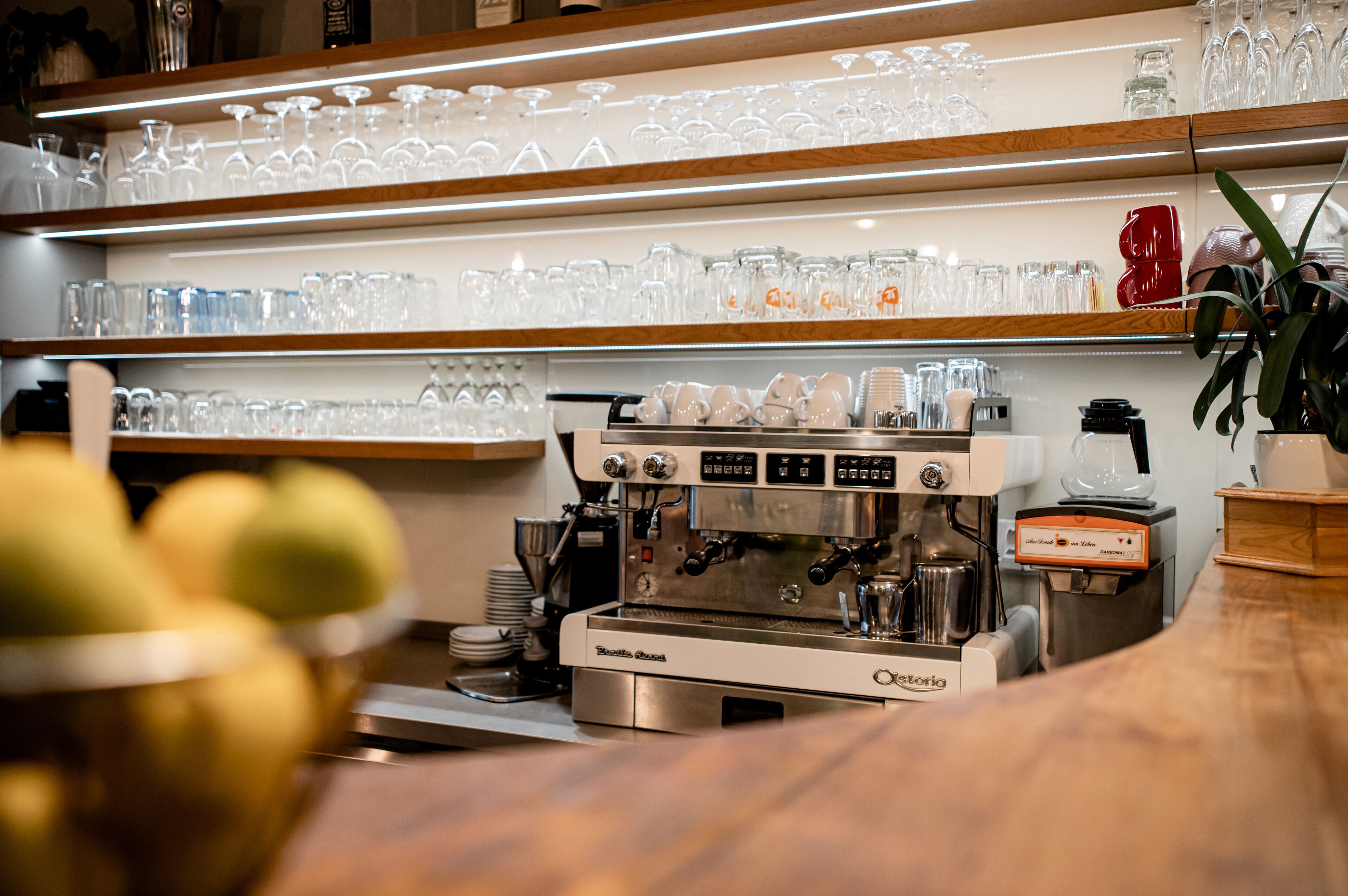 A coffee machine, glassware, and a bowl of fruit on a counter.