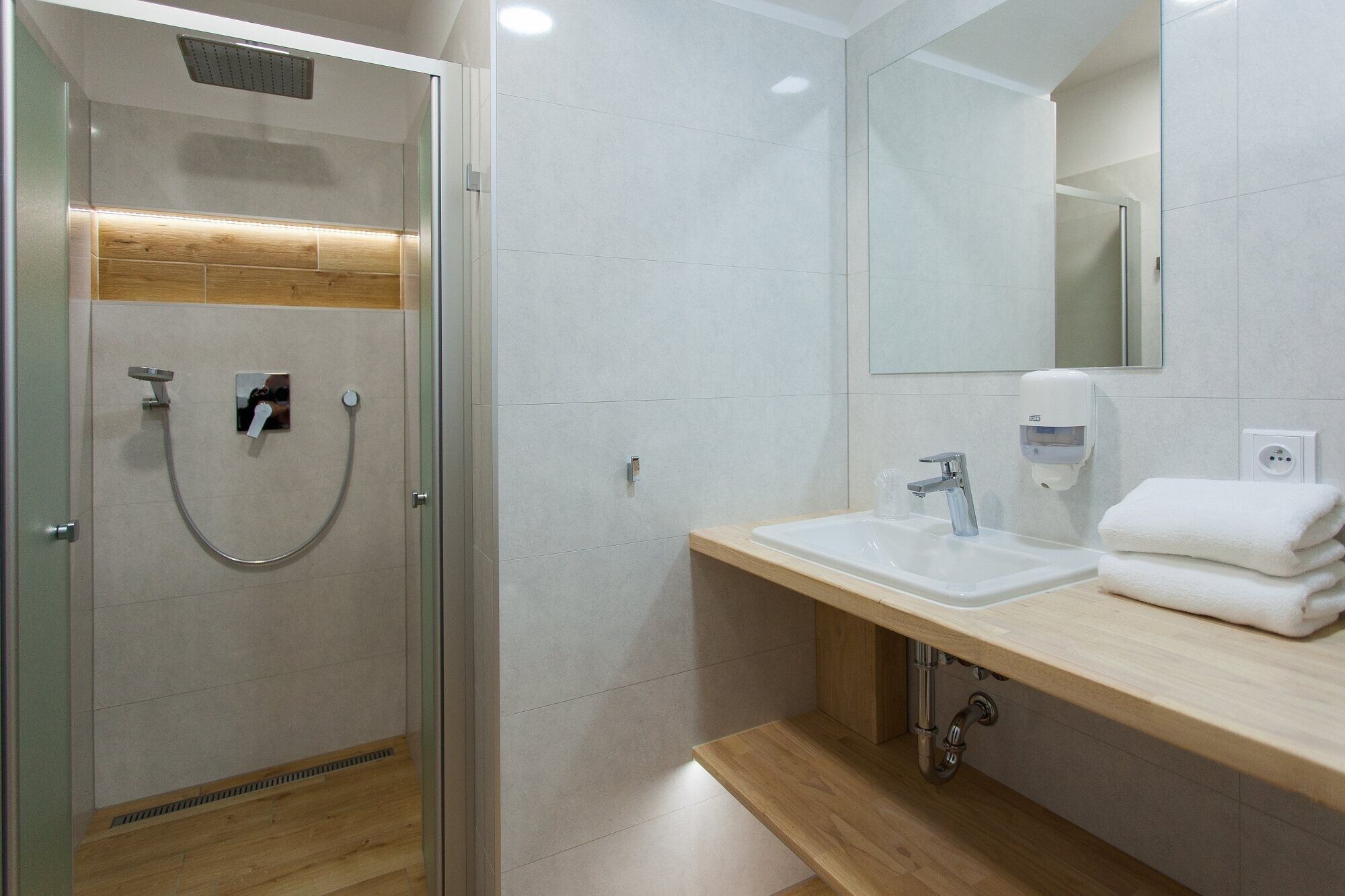 Un baño moderno con ducha de vidrio, tocador de madera con lavamanos y espejo.