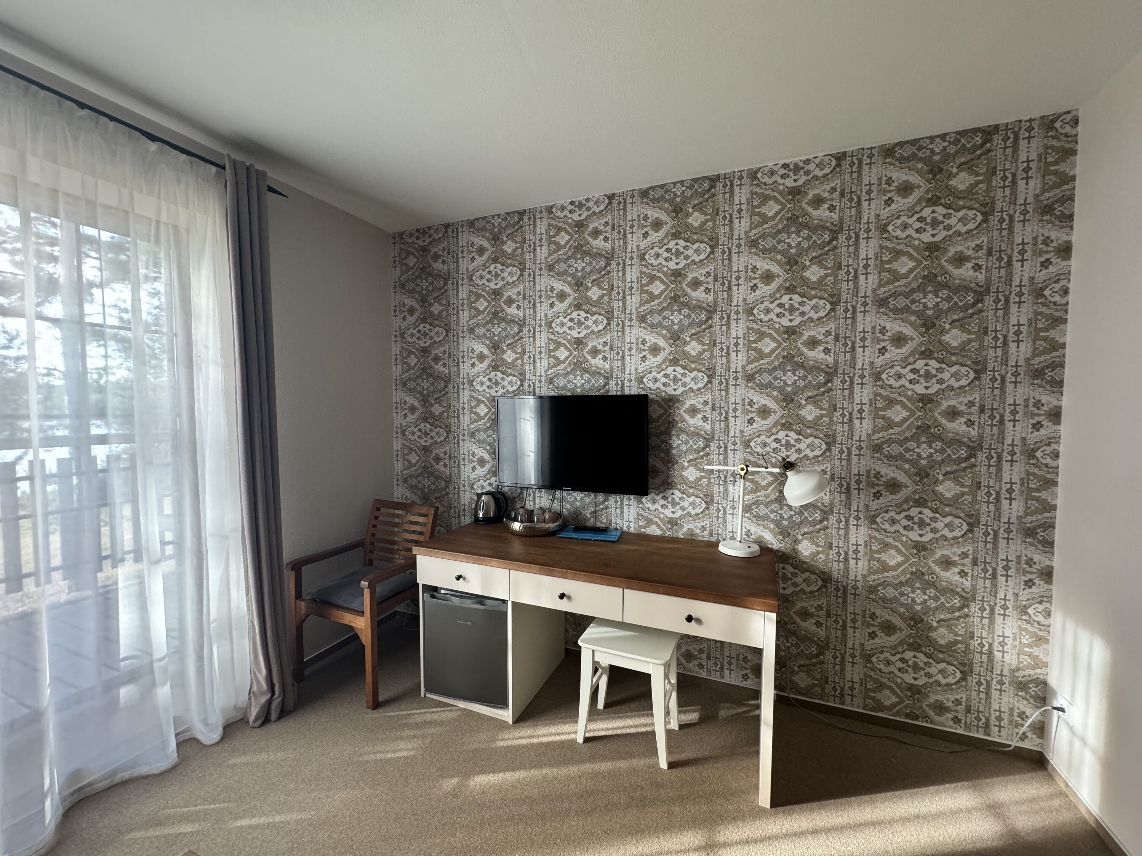 A small, neatly arranged bedroom with a single bed, a bedside table, a chair, and a TV mounted on the wall.
