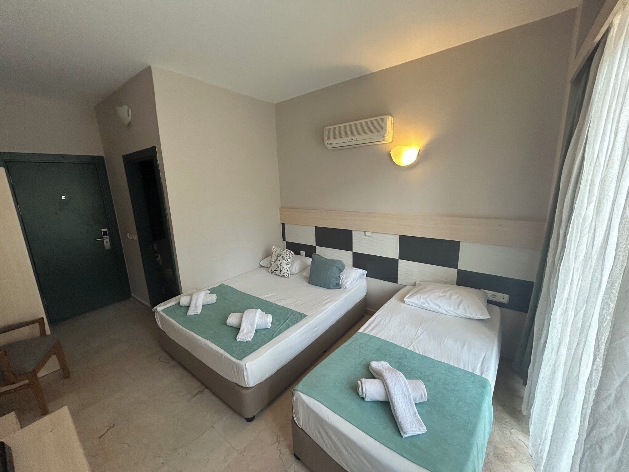 Quarto de hotel com duas camas, ar condicionado fixado na parede e uma porta.