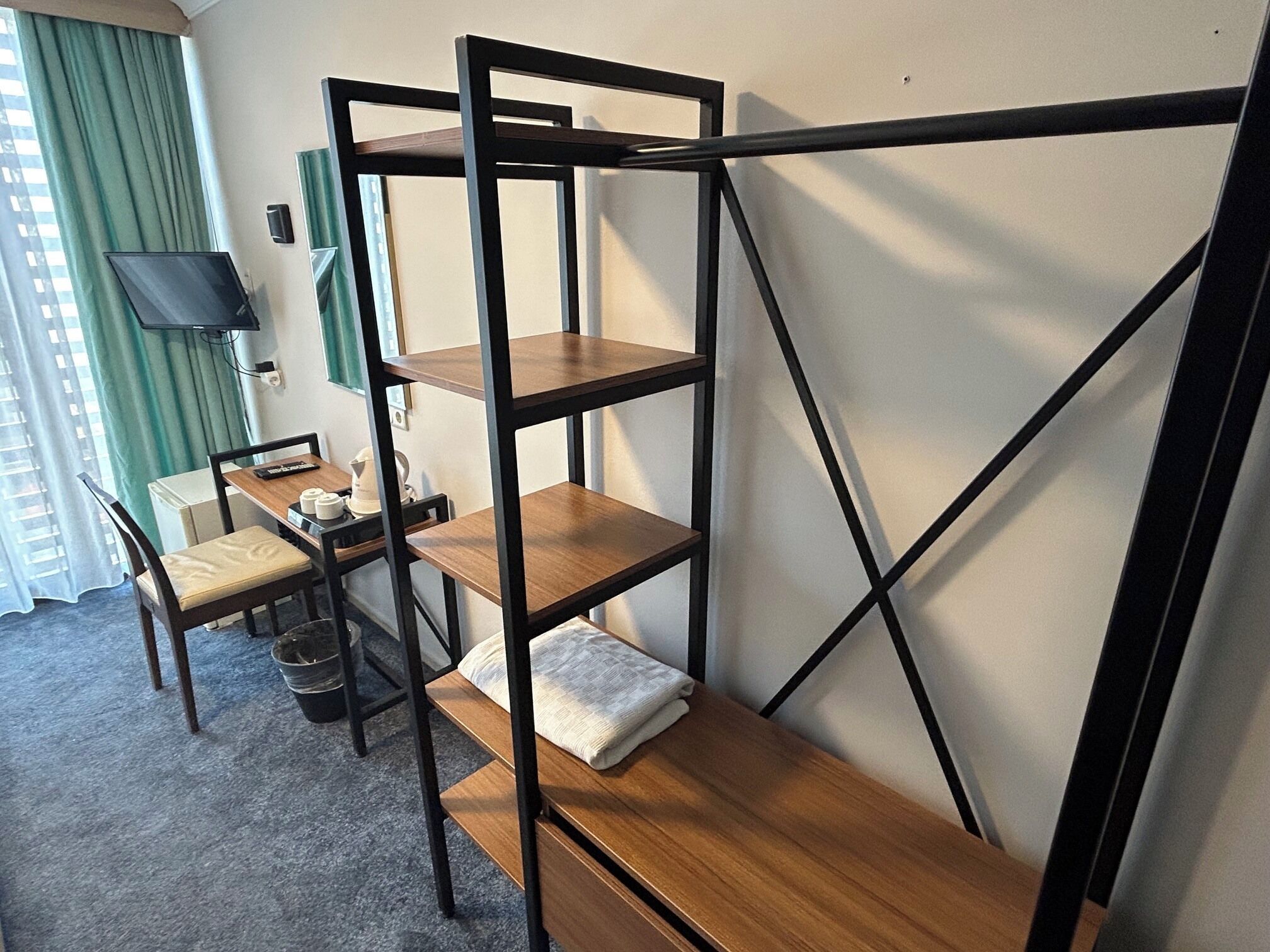 Quarto com beliche, escrivaninha com cadeira, televisão e janela com cortinas.