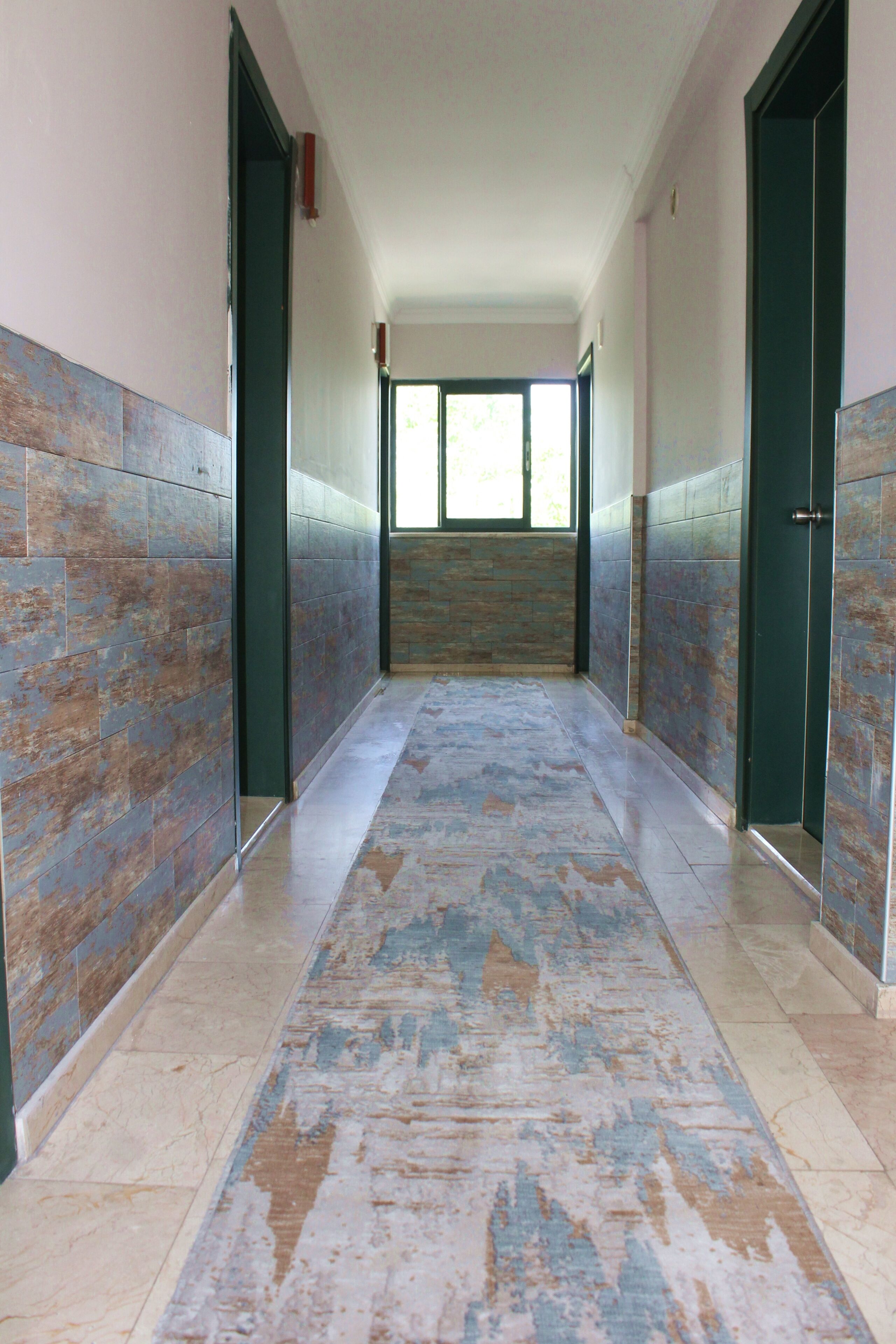 A corridor with tiled walls and a patterned carpet, leading to a door with a window at the end.