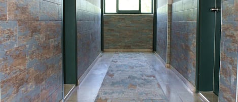 A corridor with tiled walls and a patterned carpet, leading to a door with a window at the end.