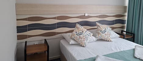 Habitación de hotel con cama, dos almohadas, mesita de noche, una silla y pared con diseño ondulado.