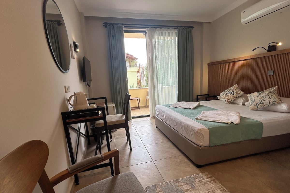 Una habitación de hotel con cama, escritorio, silla, televisor y ventana con cortinas.