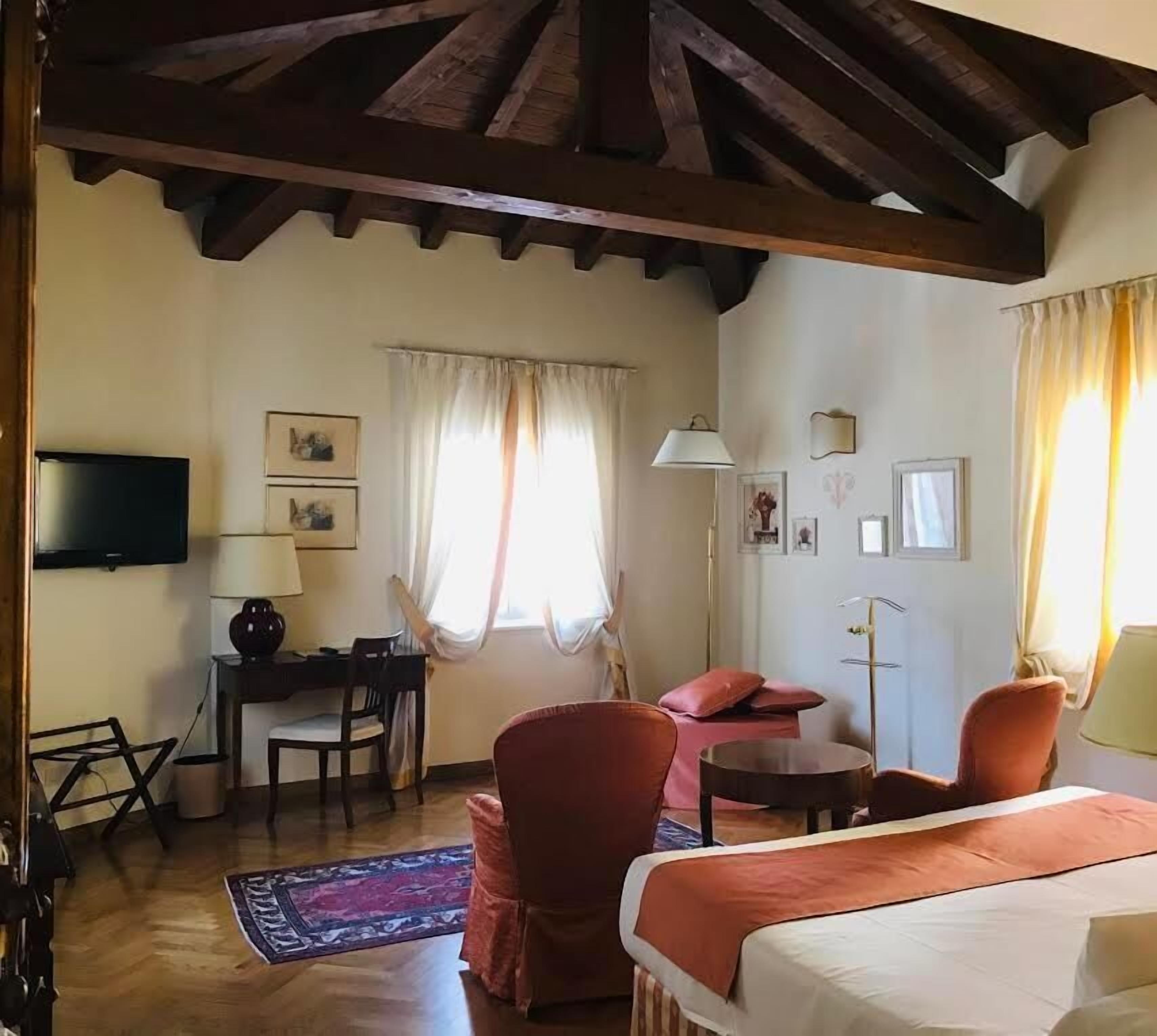 A room with a bed, a desk, a chair, a TV, and a window with curtains.