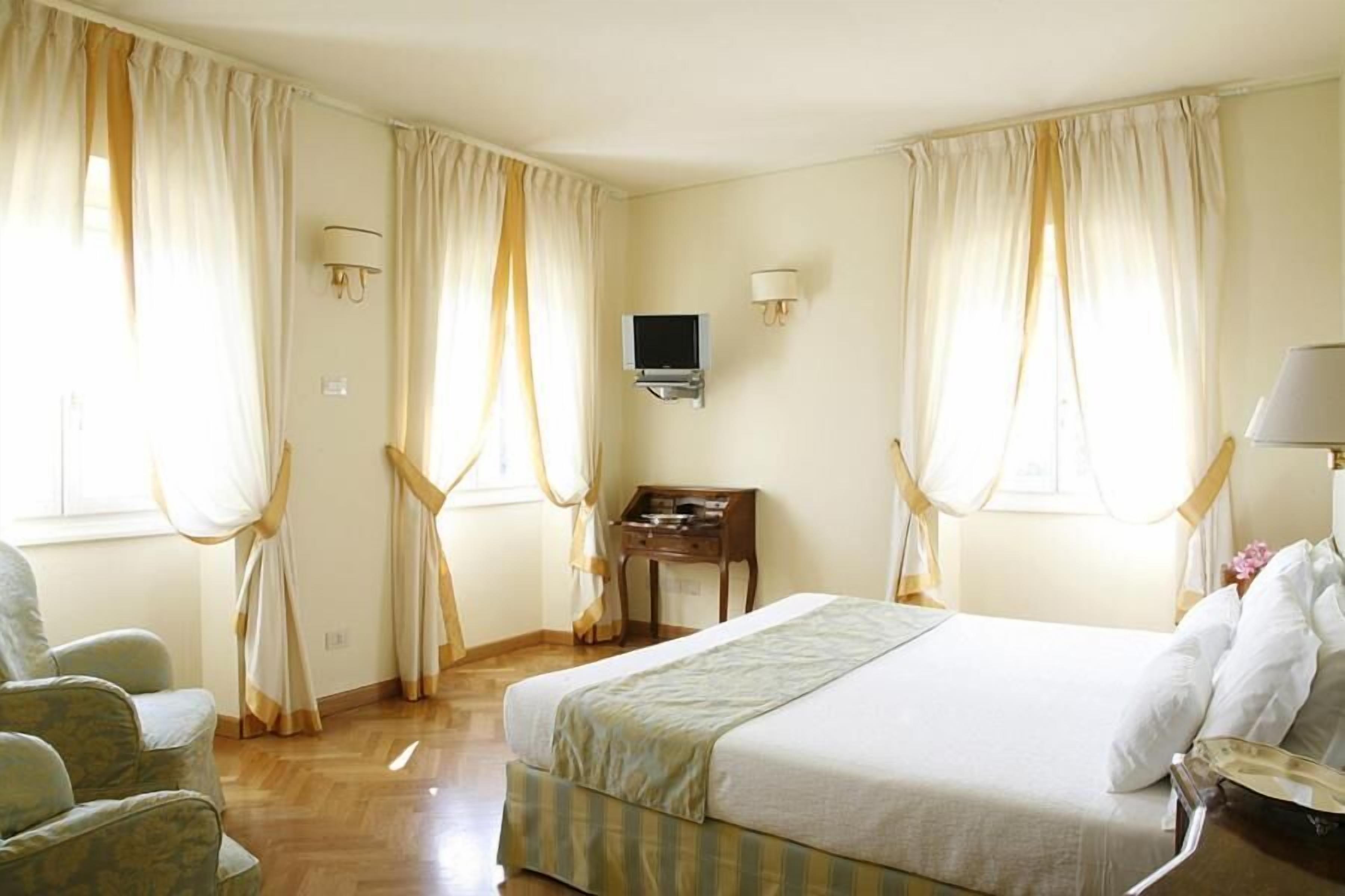 Une chambre d’hôtel avec un lit, deux chaises, un bureau, une télévision et des rideaux.