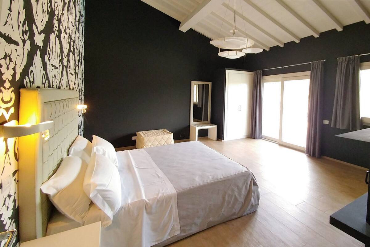 A bedroom with a bed, bedside table, lamp, and a large window with curtains.