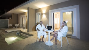 Un couple, vêtu de peignoirs, se trouve près d’une piscine extérieure chauffée, où se trouvent une table et des chaises, une petite piscine et un patio couvert.