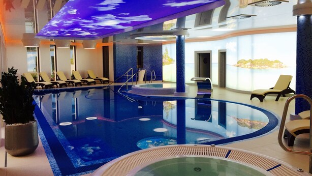 An indoor swimming pool with lounge chairs, a hot tub, and a ceiling with a sky-like design. - Grand Laola Spa (Rewal)