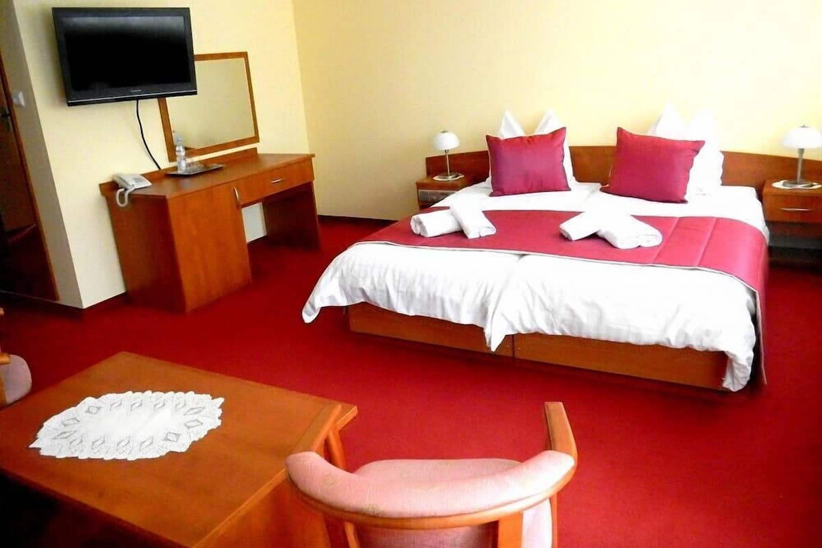 A hotel room with a bed, a desk, a chair, a TV, and bedside tables.