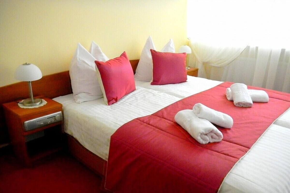 A hotel room with a bed, pillows, a nightstand, and a lamp.