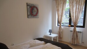 A bedroom with a bed, a bedside table with a lamp, a window with curtains, and a wall with a painting. - Apartment Gurguliat Sofia (Sofia)