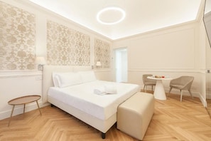 A hotel room with a bed, a small round table, two chairs, a lamp, and a door. - Alexander (Assisi)