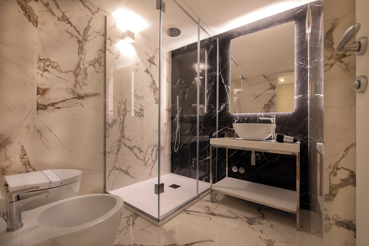 A modern bathroom with a glass-enclosed shower, a white sink, and a marble-tiled wall.