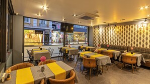 A restaurant with tables covered in yellow and grey tablecloths, wicker chairs, and a patterned wall. - Neda  (Istanbul)