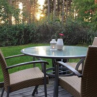 A round glass table with wicker chairs, a white lantern, and a vase with a pink flower.