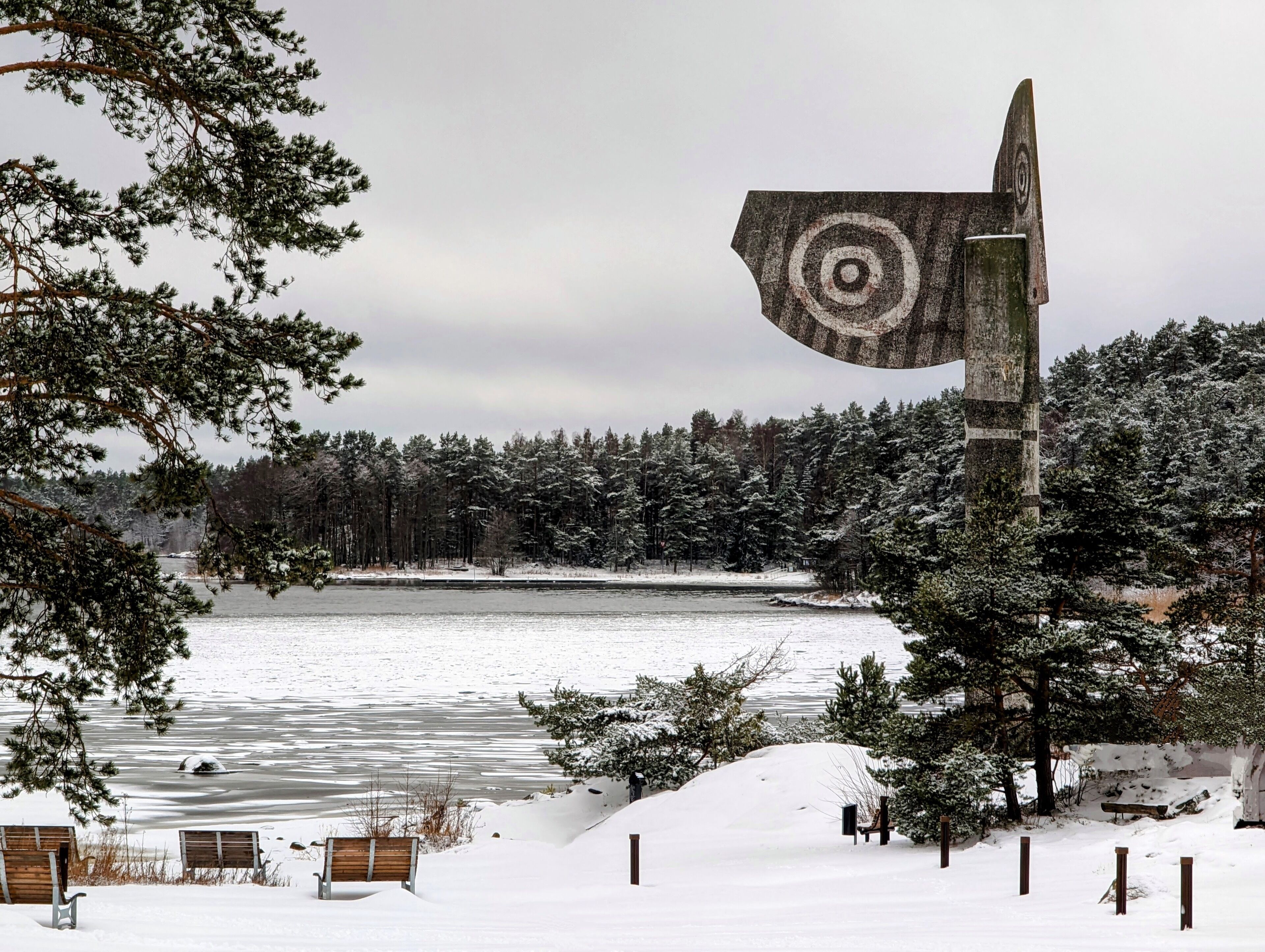 A snowy landscape with a lake, trees, and a large sculpture.