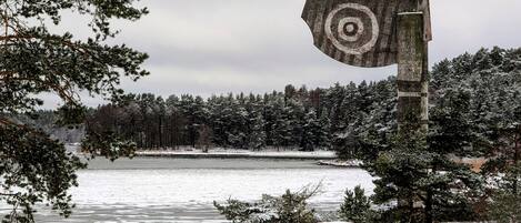 A snowy landscape with a lake, trees, and a large sculpture.