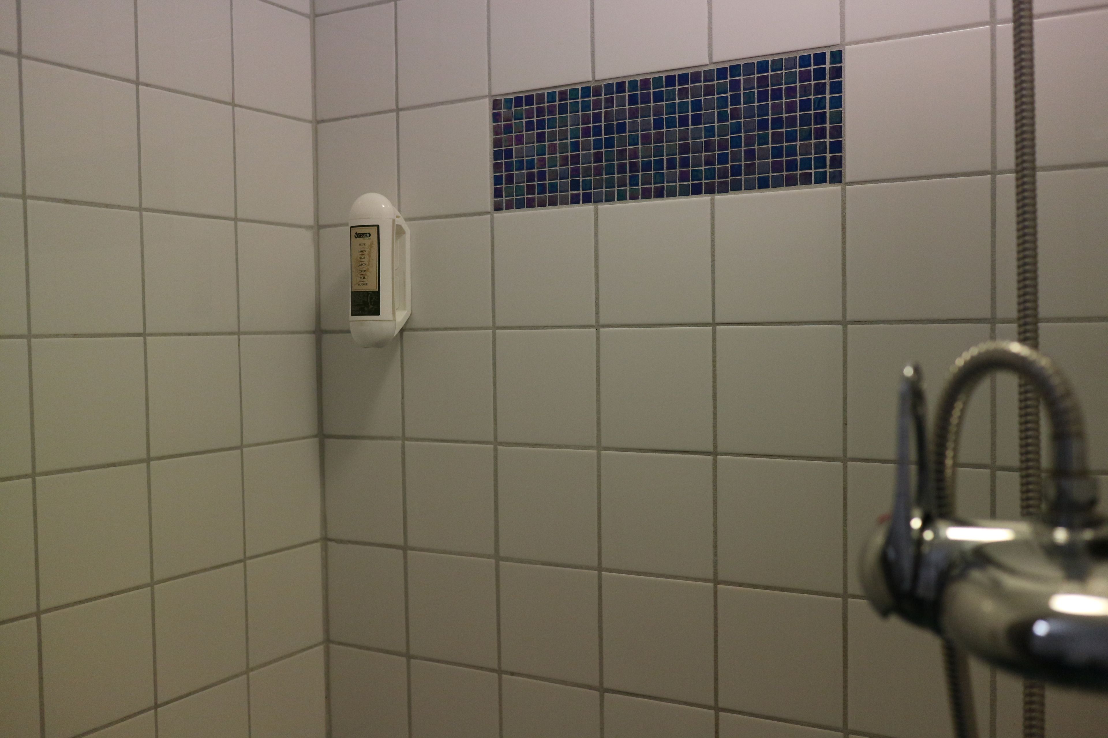 Zona de ducha con azulejos, un cabezal de ducha de mano y un panel digital de control de temperatura.