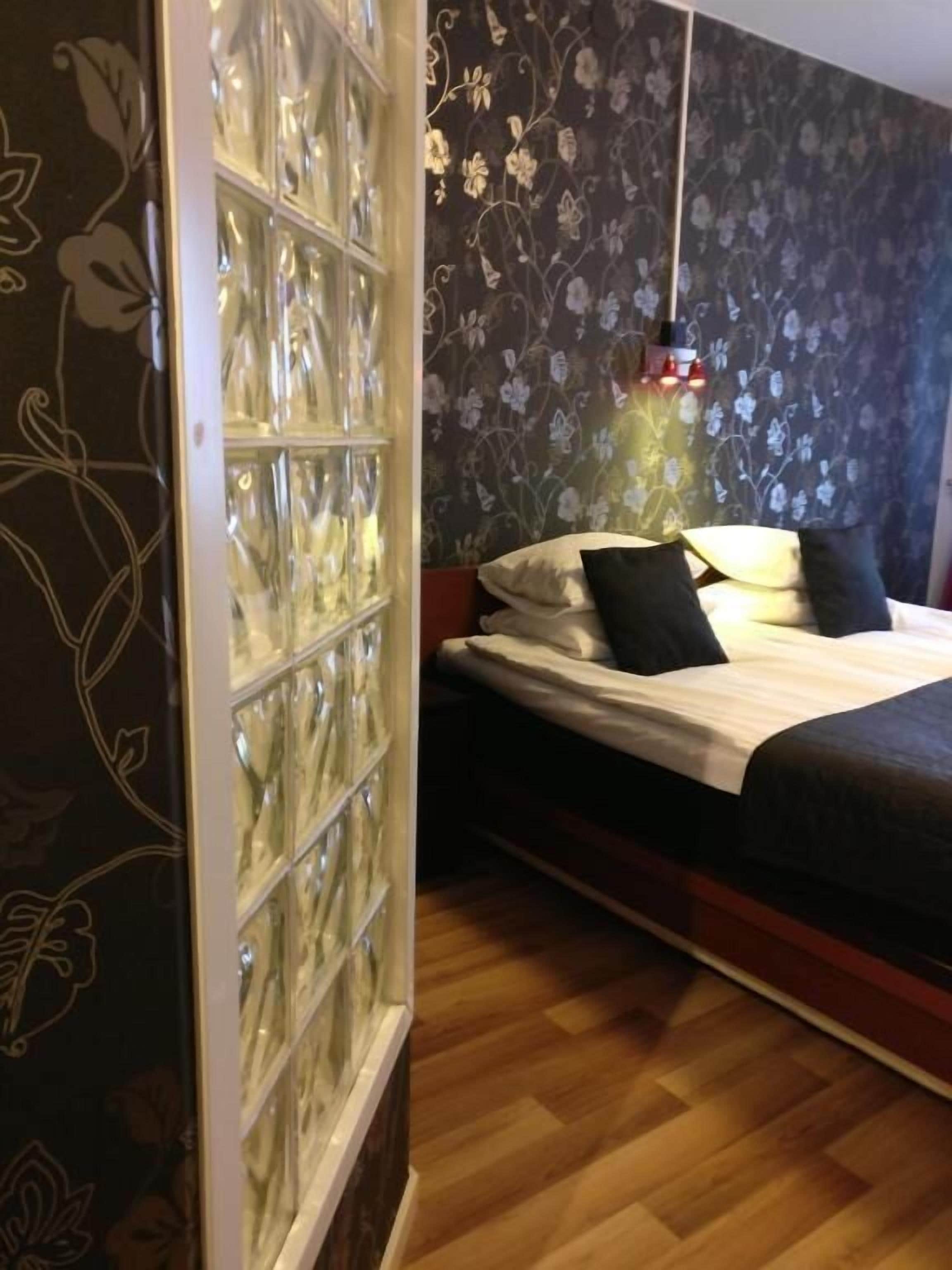 Un dormitorio con cama, mesita de noche, lámpara de pared y un aparador de vidrio decorativo.