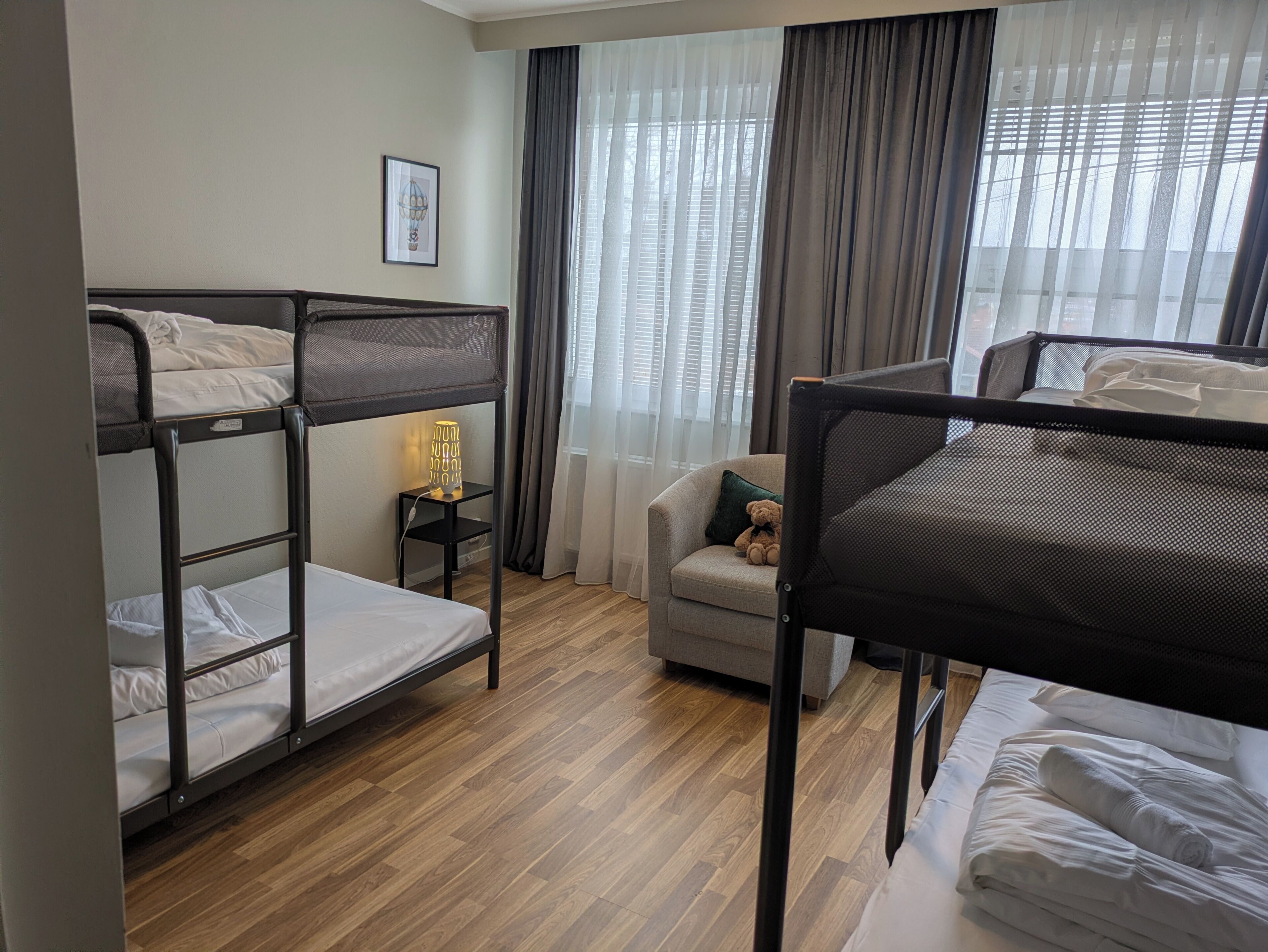 Habitación de hotel con literas, un pequeño sofá, un osito de peluche, una lámpara y un cuadro en la pared.