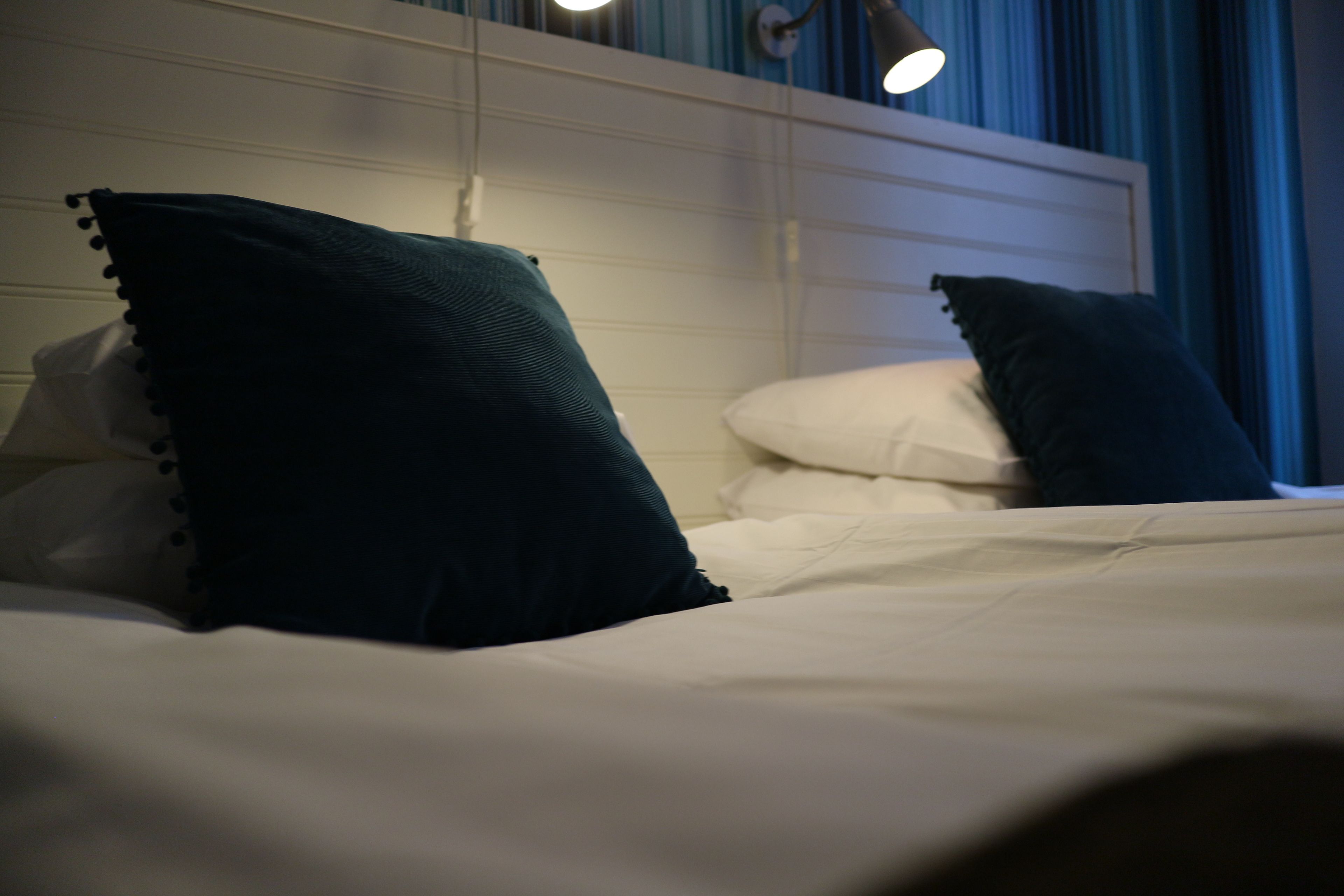 A neatly made bed with white linens and dark green pillows.