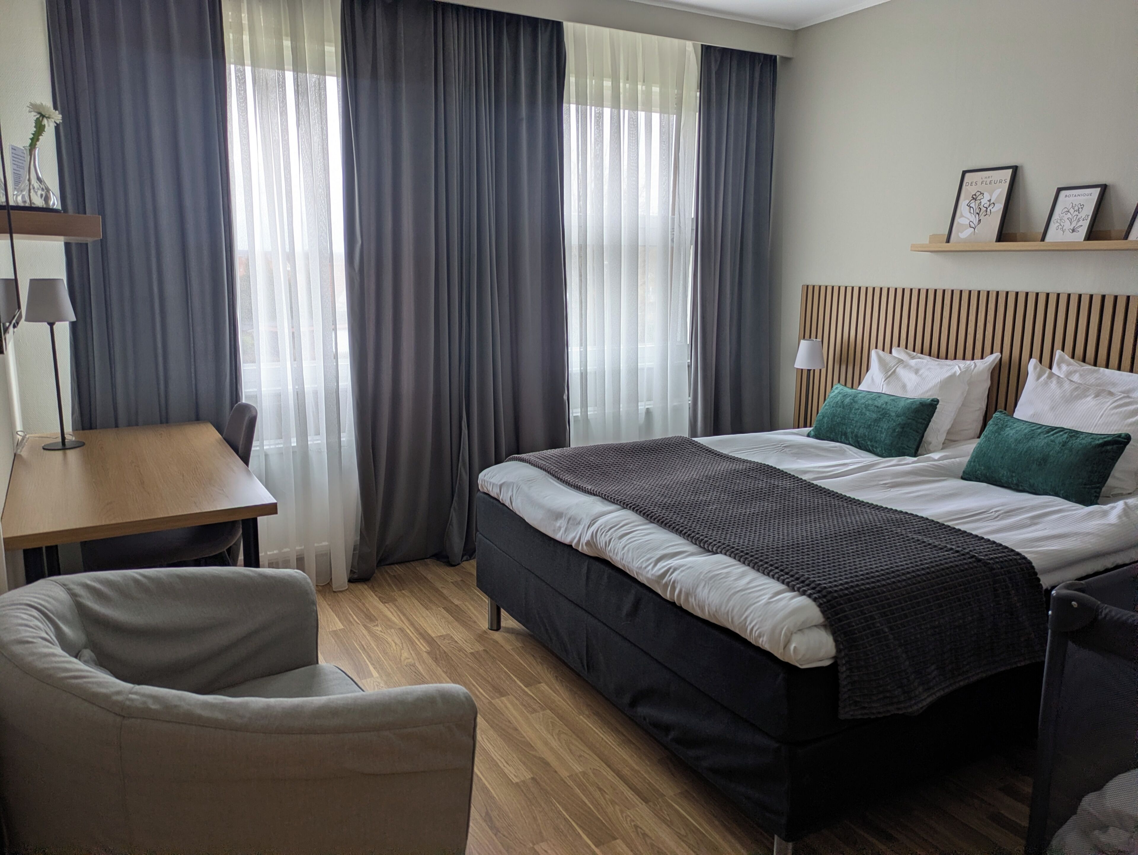 A hotel room with a bed, a chair, a desk, and a window with curtains.
