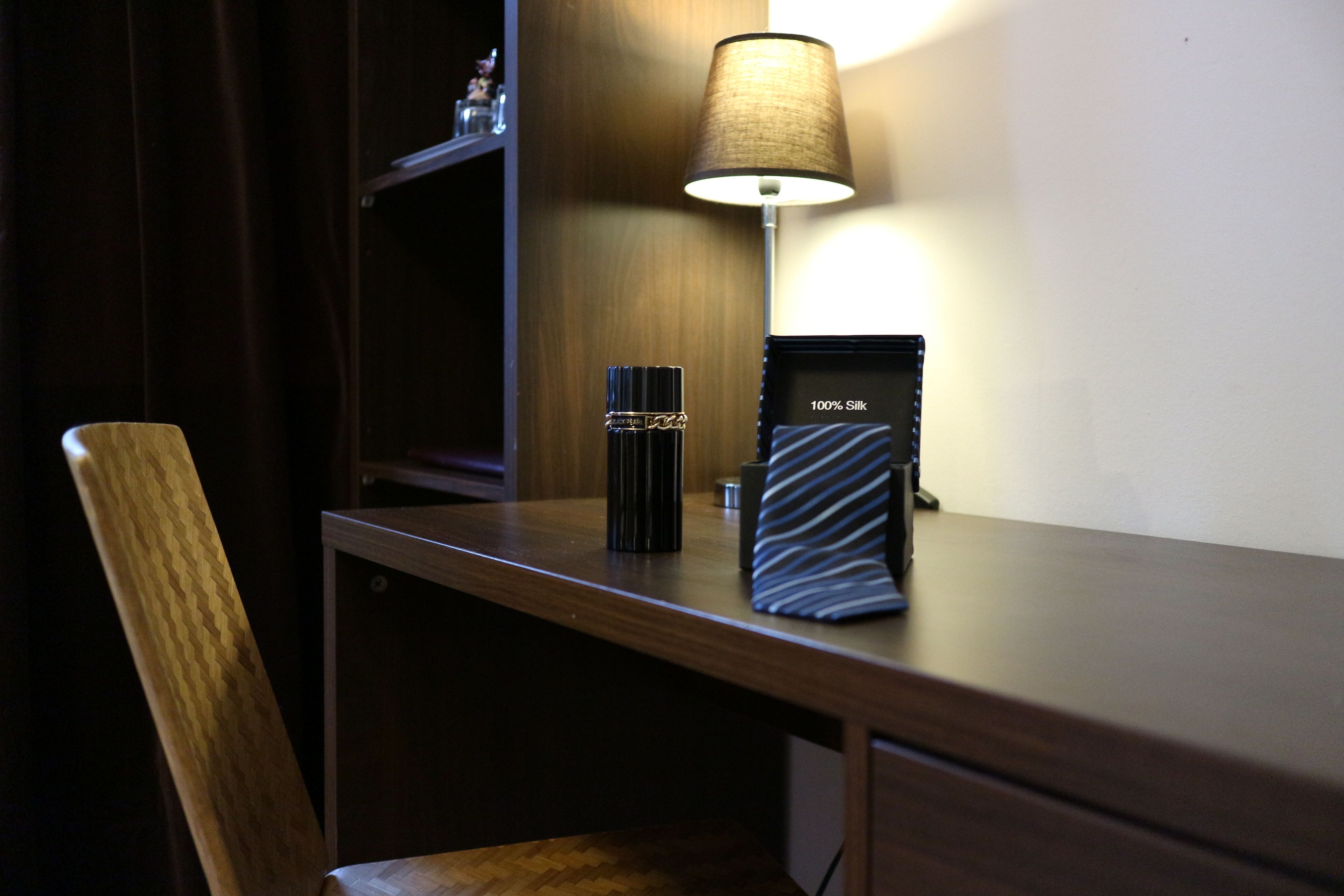 A wooden desk with a lamp, a black cylindrical object, and a pillow.
