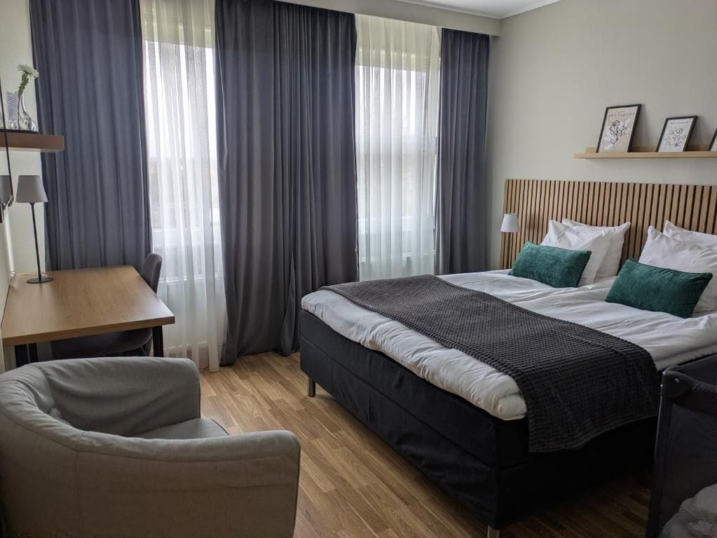 A hotel room with a bed, a desk, a chair, and a window with curtains.