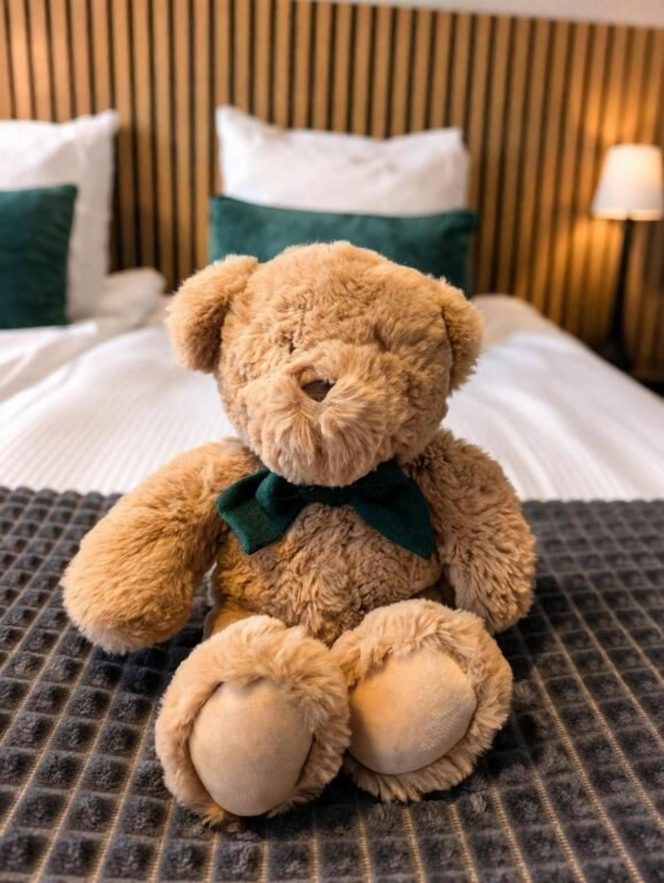 A plush teddy bear with a bow on a bed with a striped headboard and pillows.