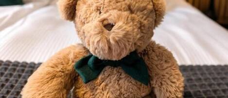 A plush teddy bear with a bow on a bed with a striped headboard and pillows.