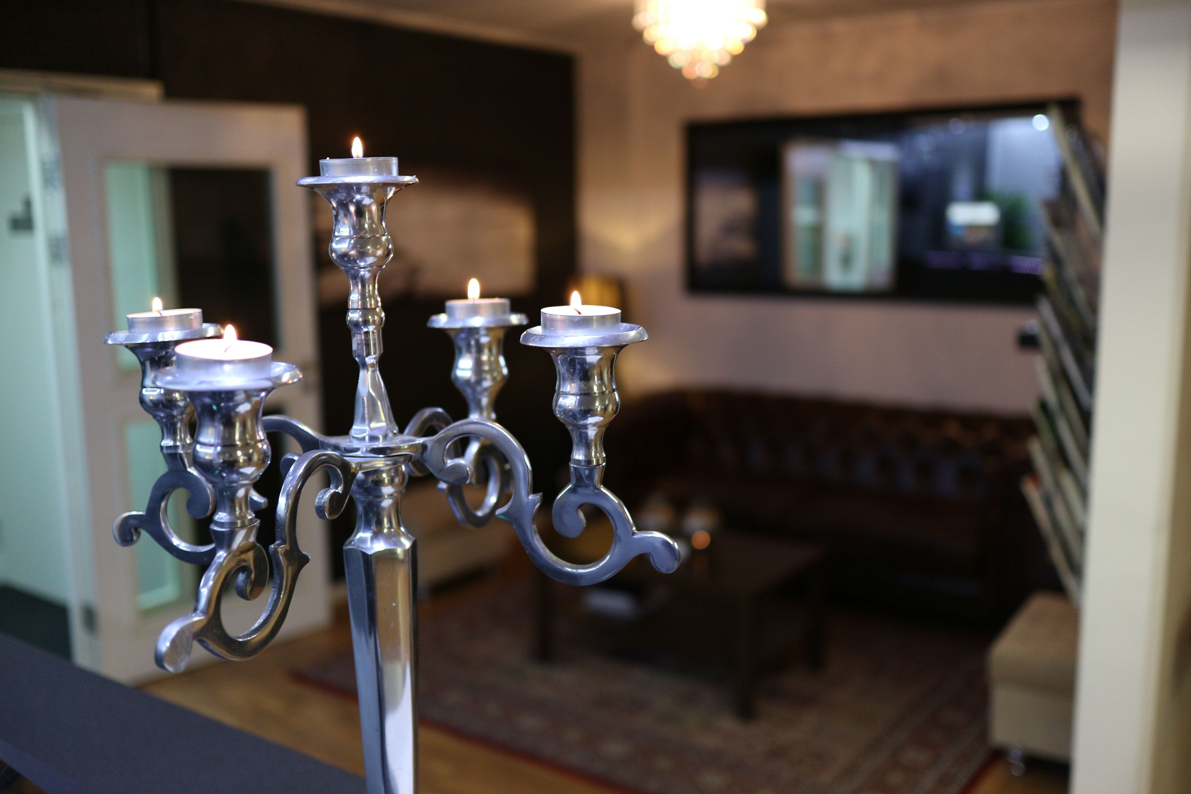 A chandelier with multiple candle-like lights in a room with a sofa and a television in the background.