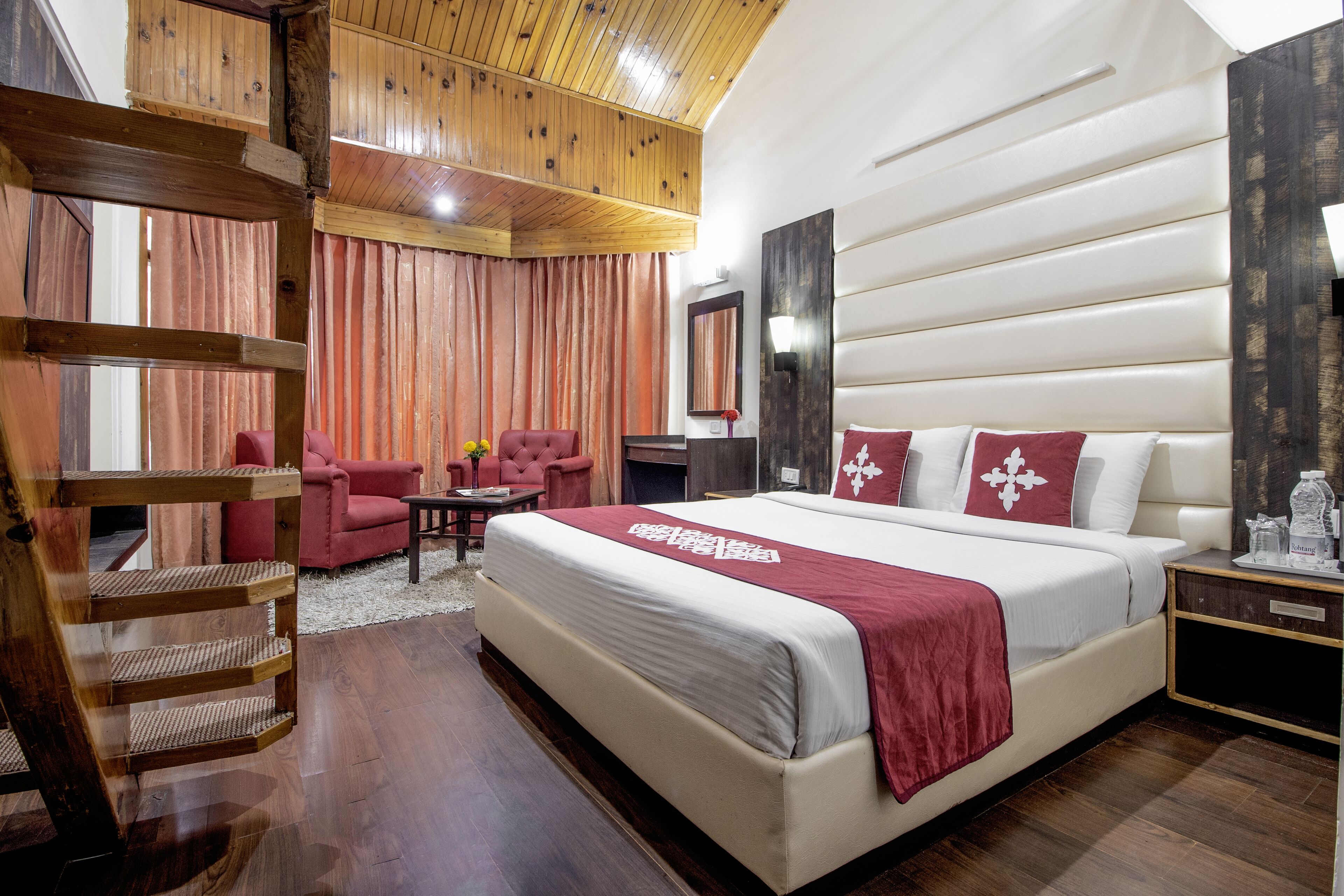 A spacious bedroom with a large bed, wooden ceiling, and a red chair.