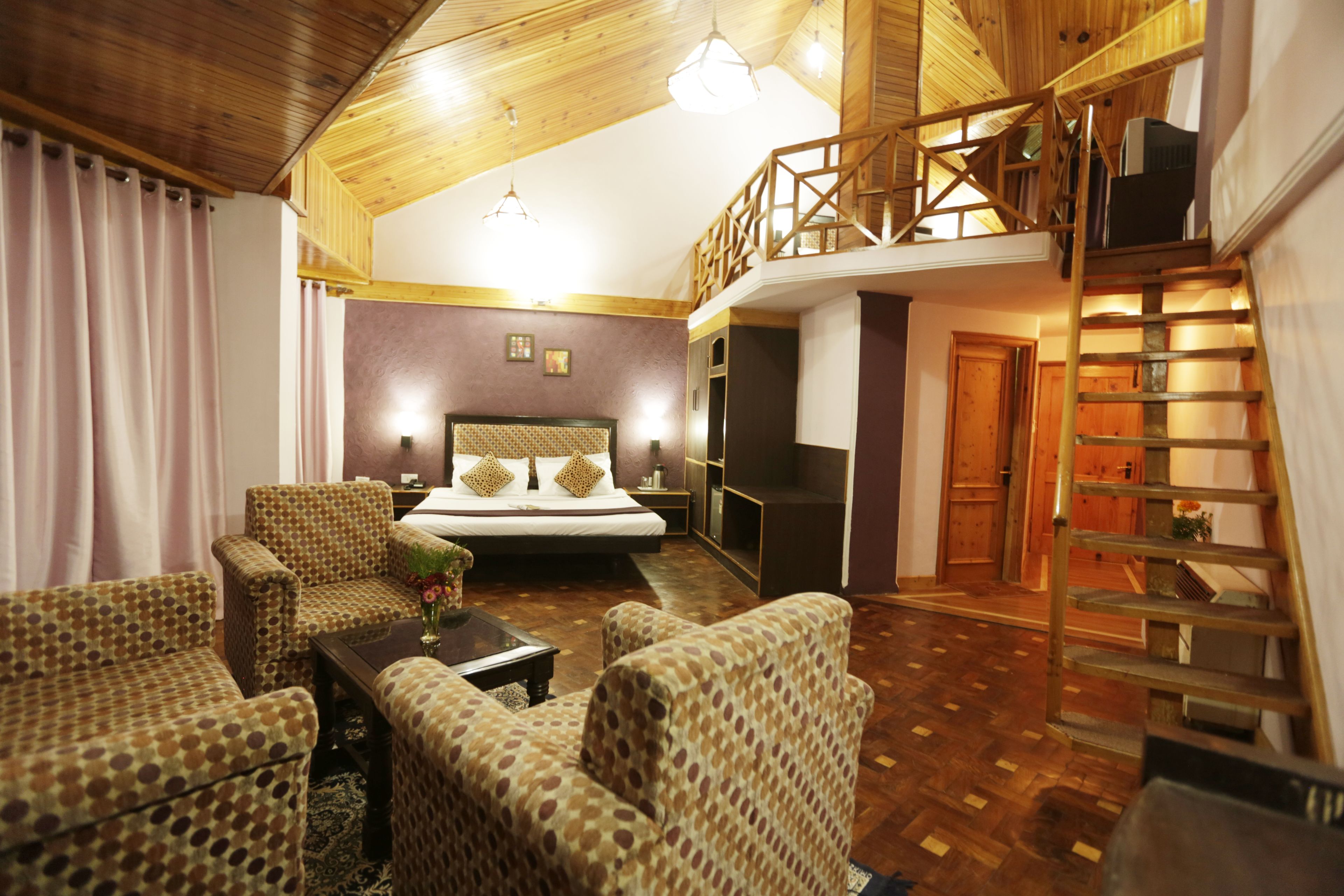 Una habitación amplia con una cama grande, dos sillones, una mesa de centro y una escalera de madera.