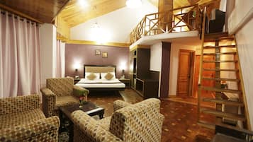 Una habitación amplia con una cama grande, dos sillones, una mesa de centro y una escalera de madera.