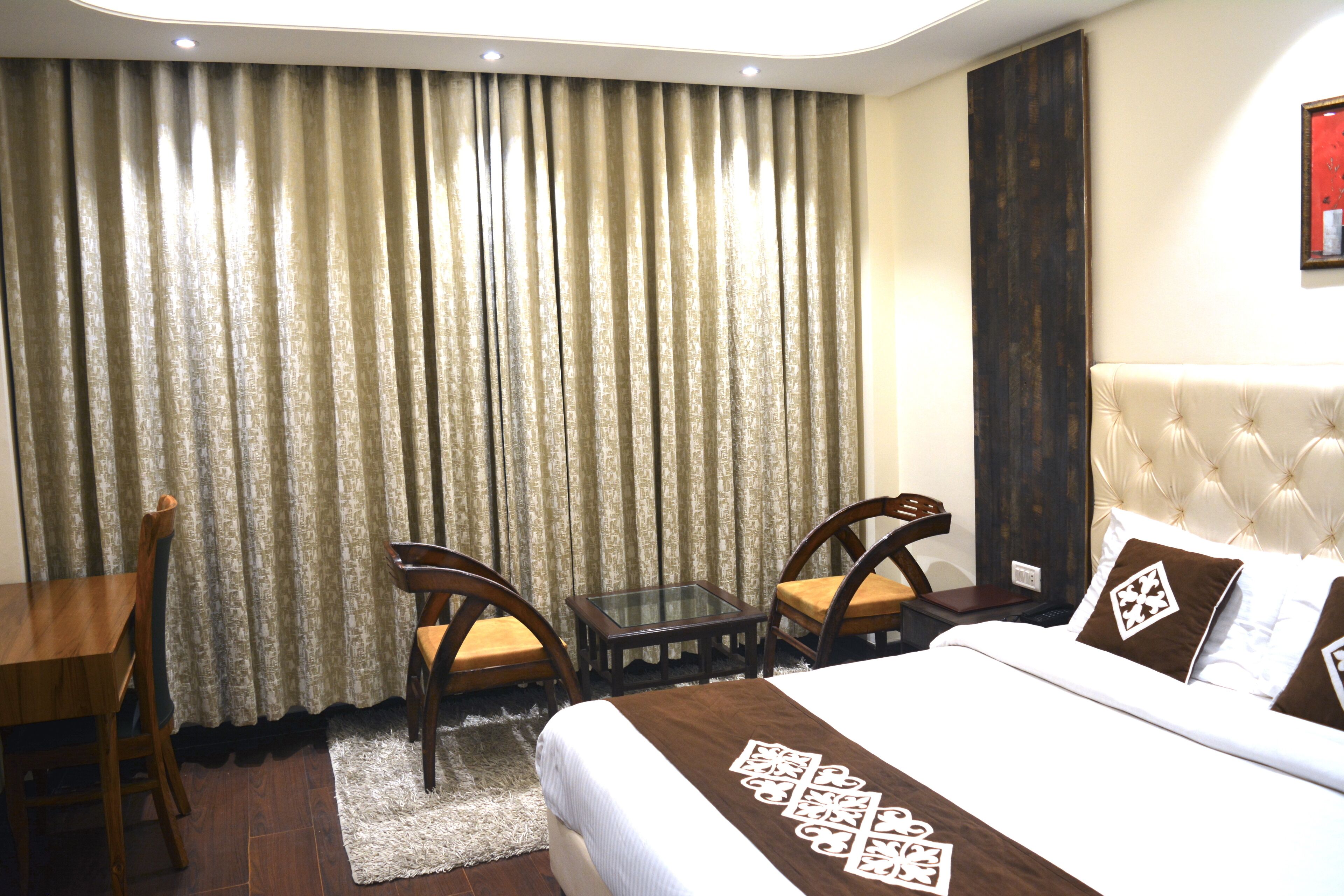 A hotel room with a bed, two chairs, a small table, and a curtain.