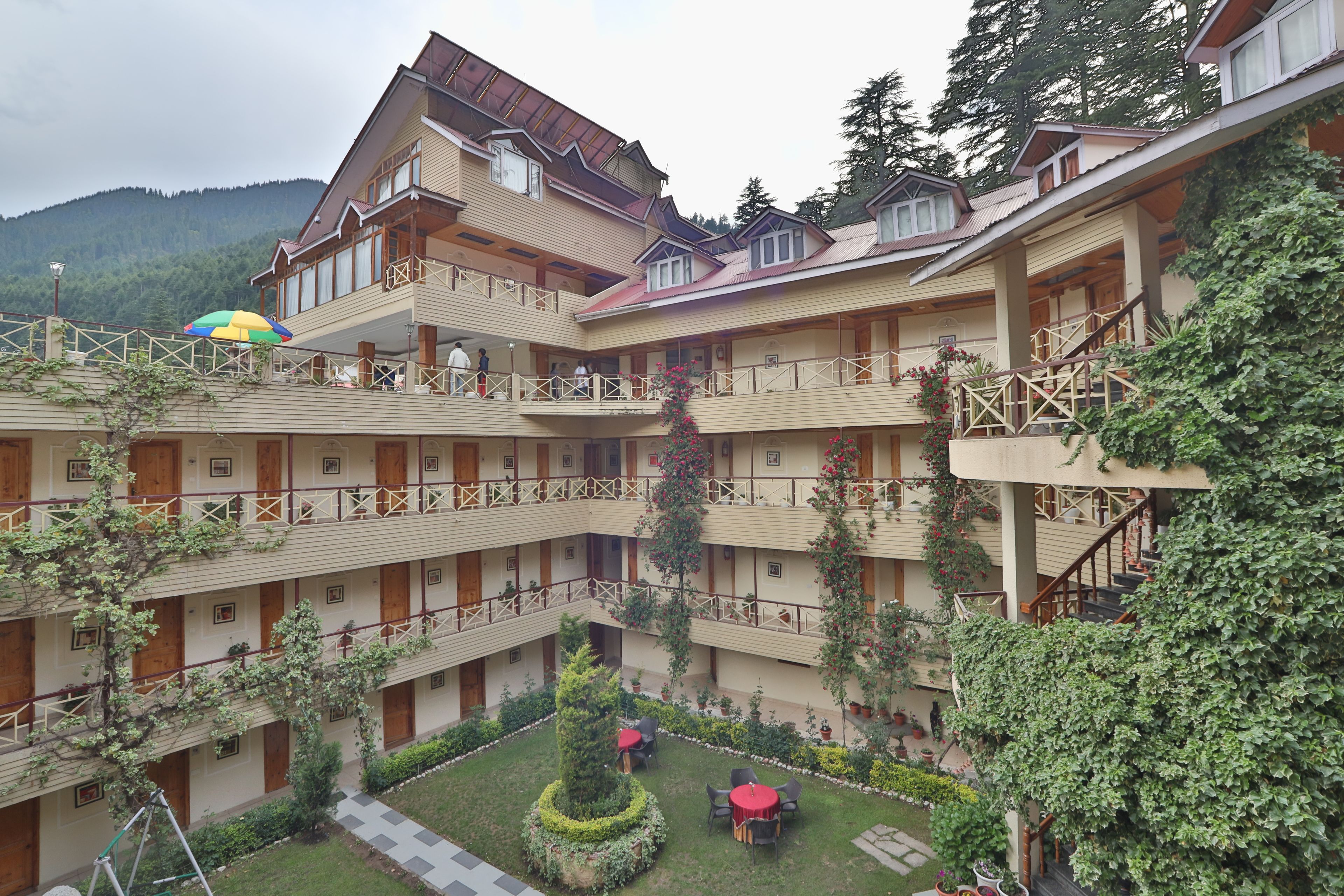 A multi-story hotel with balconies, a courtyard with seating, and a mountainous backdrop.