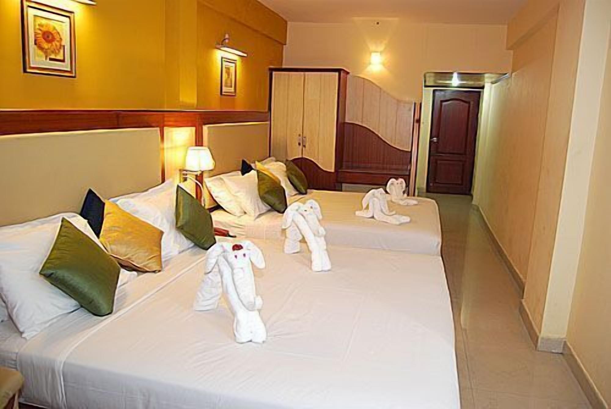 Habitación de hotel con dos camas, cada una con ropa de cama y almohadas blancas, una lámpara de noche y un cuadro en la pared.