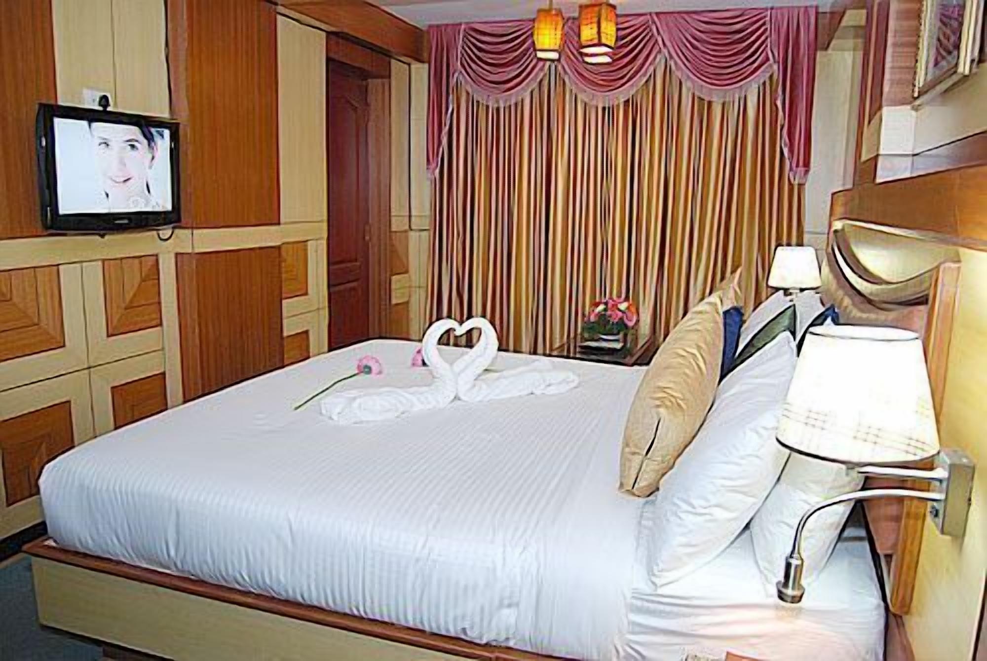 Quarto de hotel com uma cama grande, uma televisão na parede e uma cortina com listras verticais.