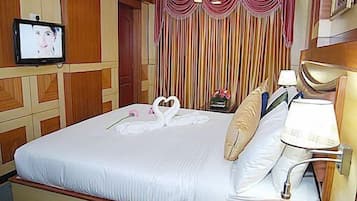Quarto de hotel com uma cama grande, uma televisão na parede e uma cortina com listras verticais.