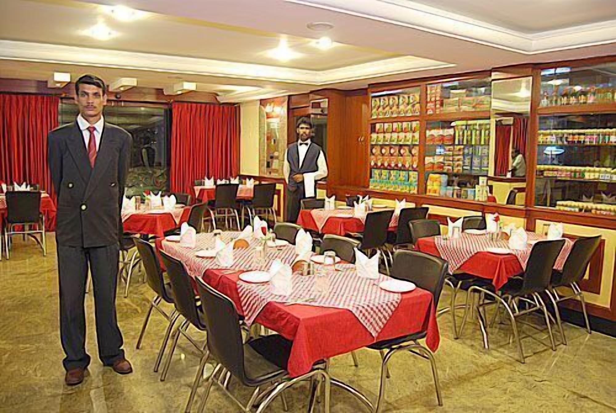 Un restaurant avec des tables dressées, un serveur en attente et un bar visible à travers une paroi en verre.