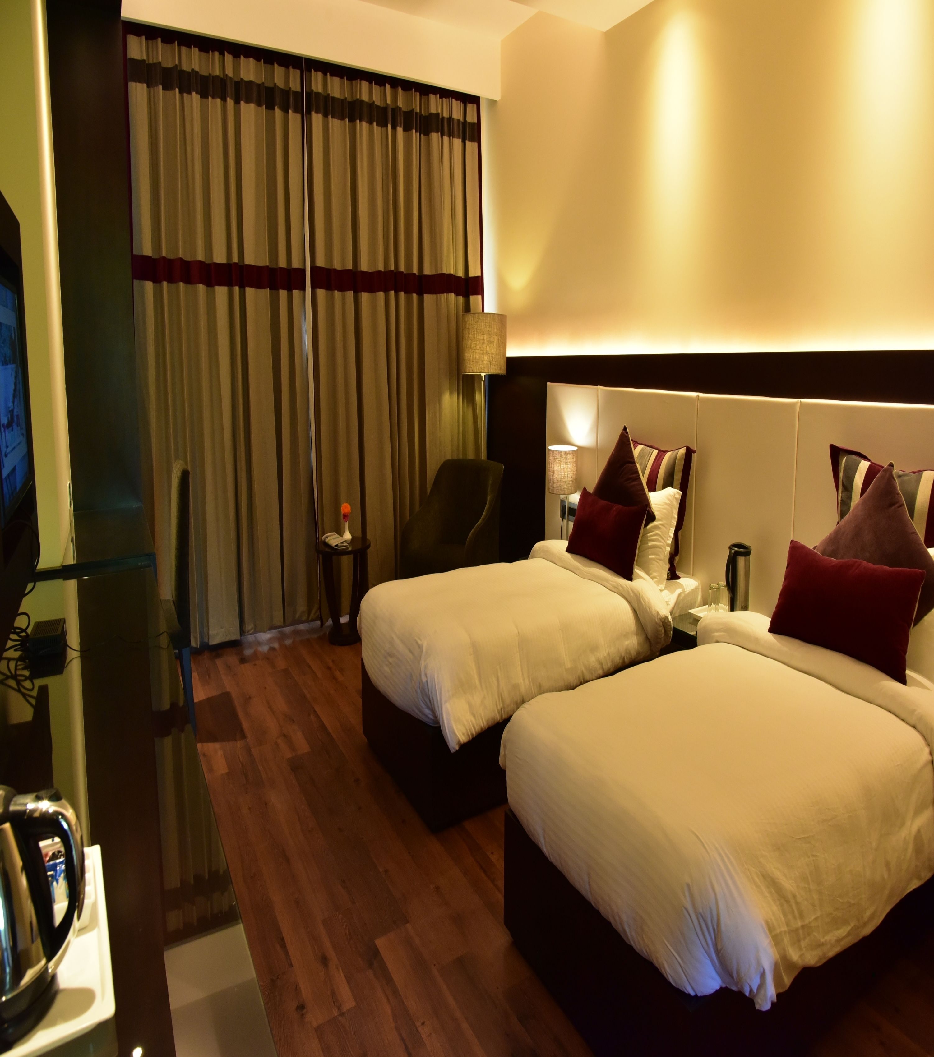 A hotel room with two beds, a TV, a lamp, and a minibar.
