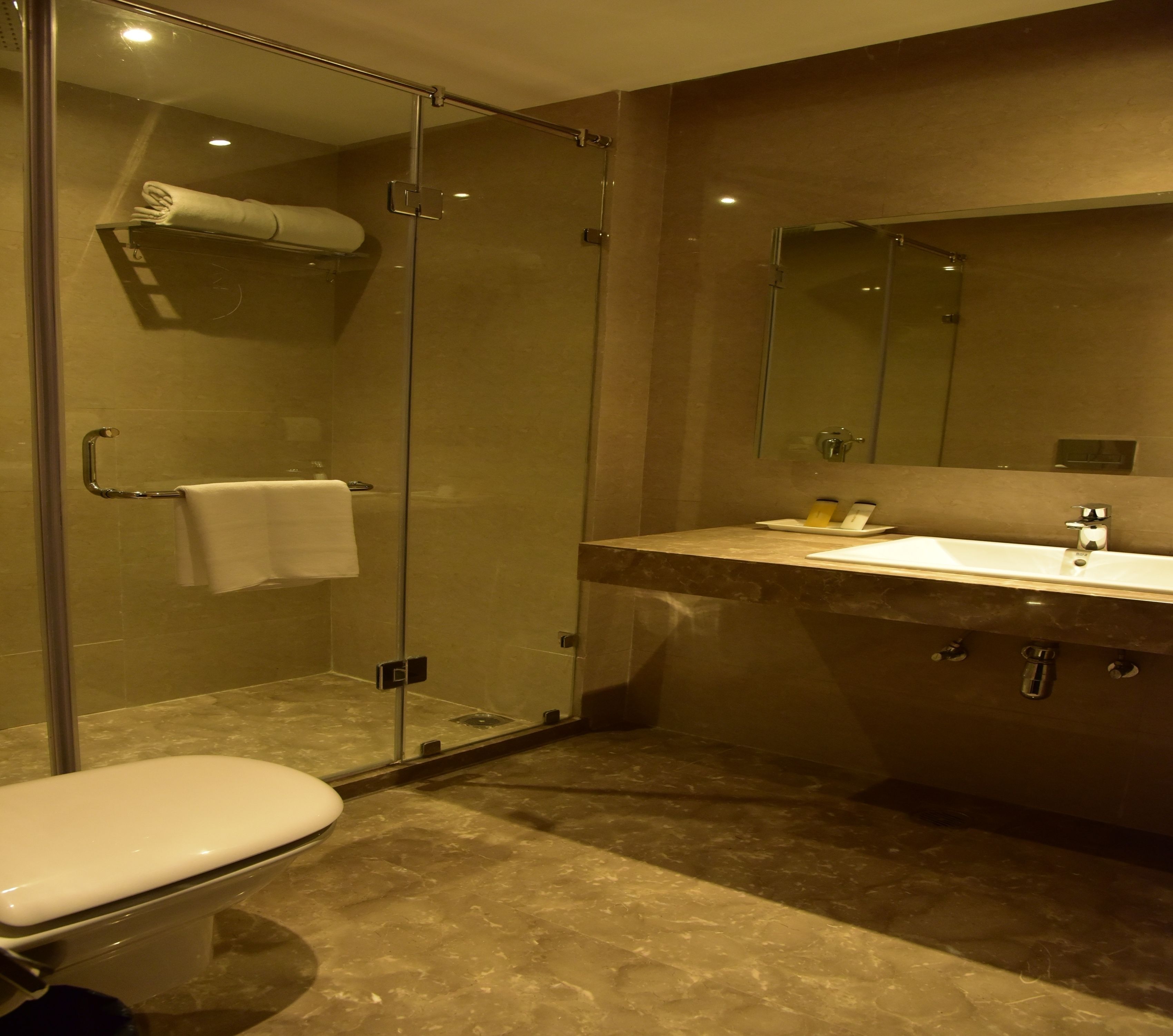 A modern bathroom with a glass-enclosed shower, a white toilet, and a marble countertop with a sink and mirror.