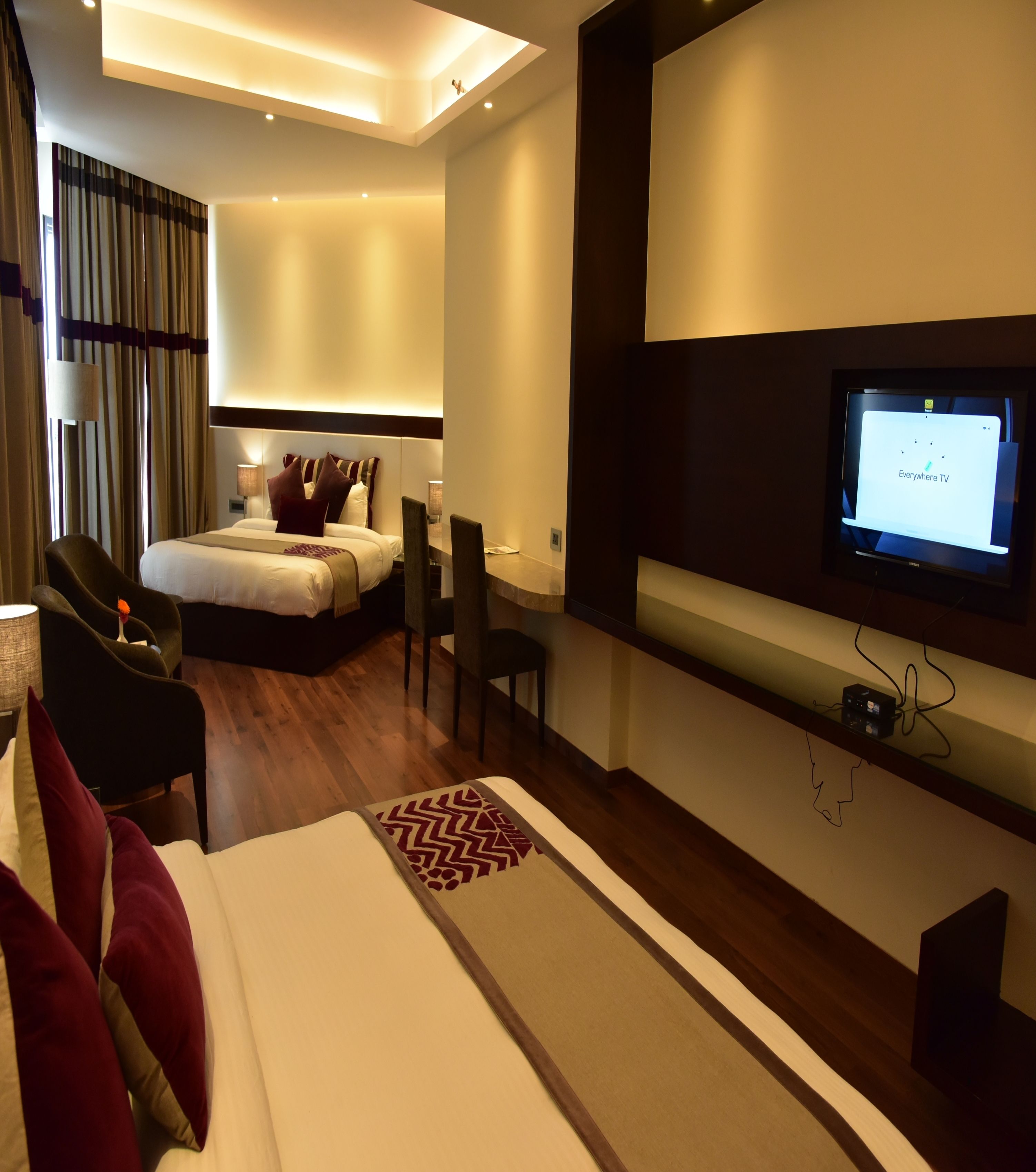 A modern hotel room with a bed, a desk, a chair, a TV, and a large window with curtains.