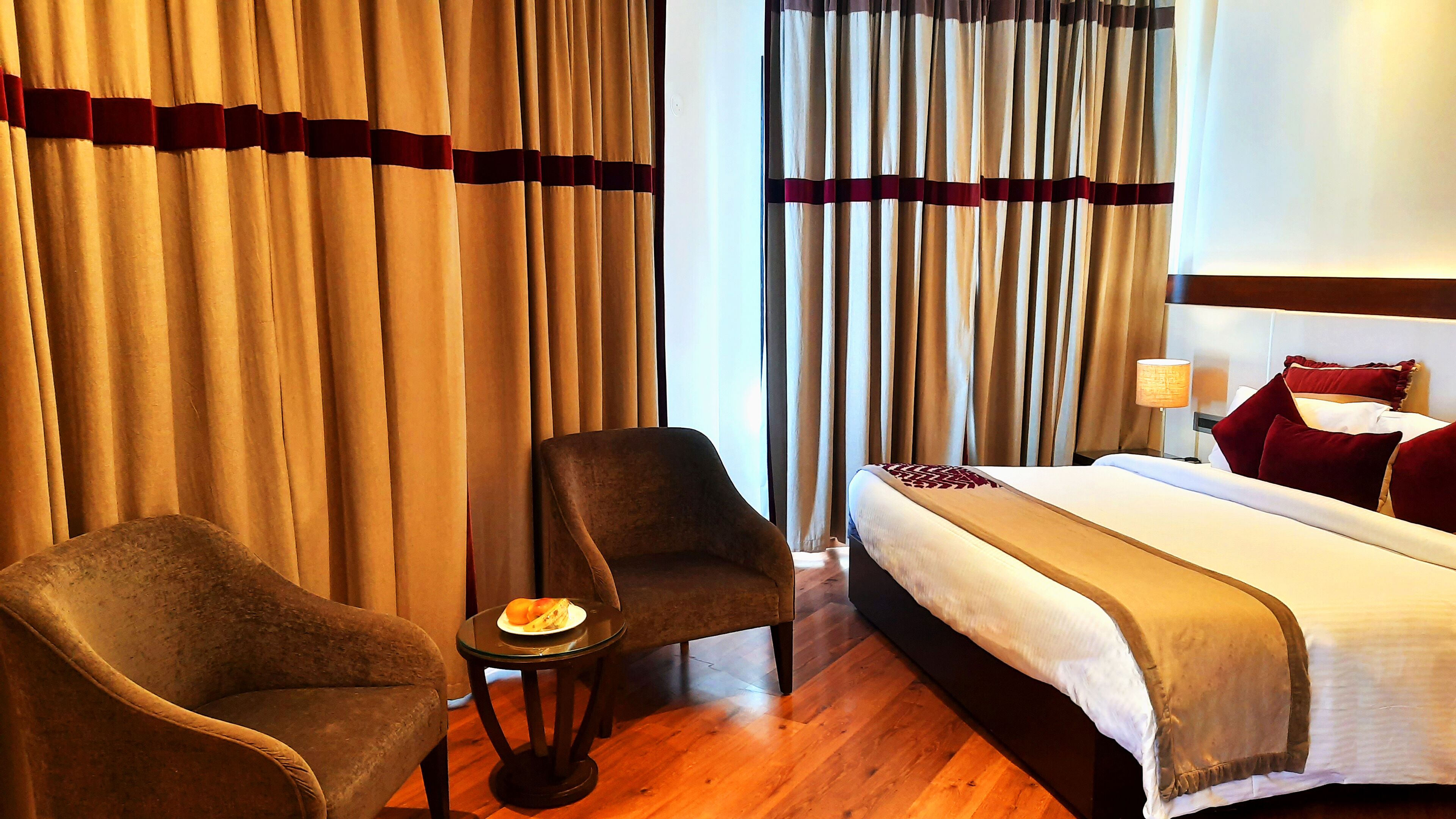 A hotel room with a bed, two armchairs, a small table with a plate, and curtains.